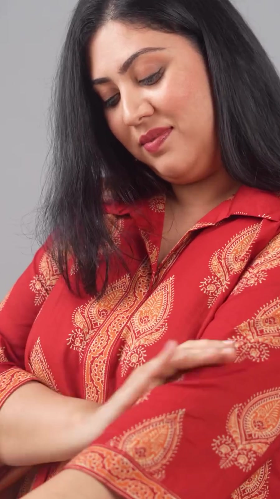 A plus-size model smiling down at the sleeve of her red Ammu co-ord set