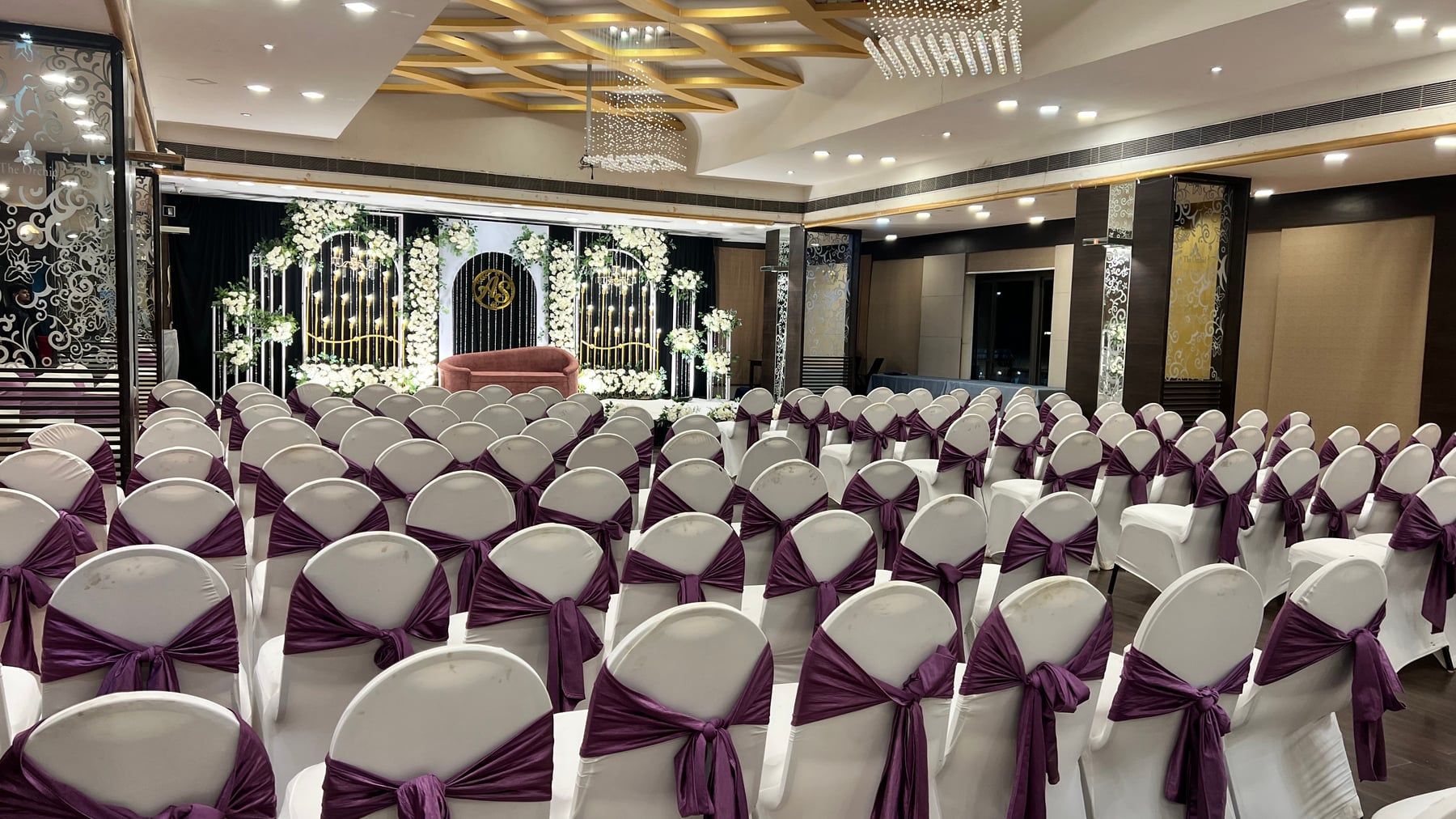 Banquet chairs with plum sashes facing a floral stage