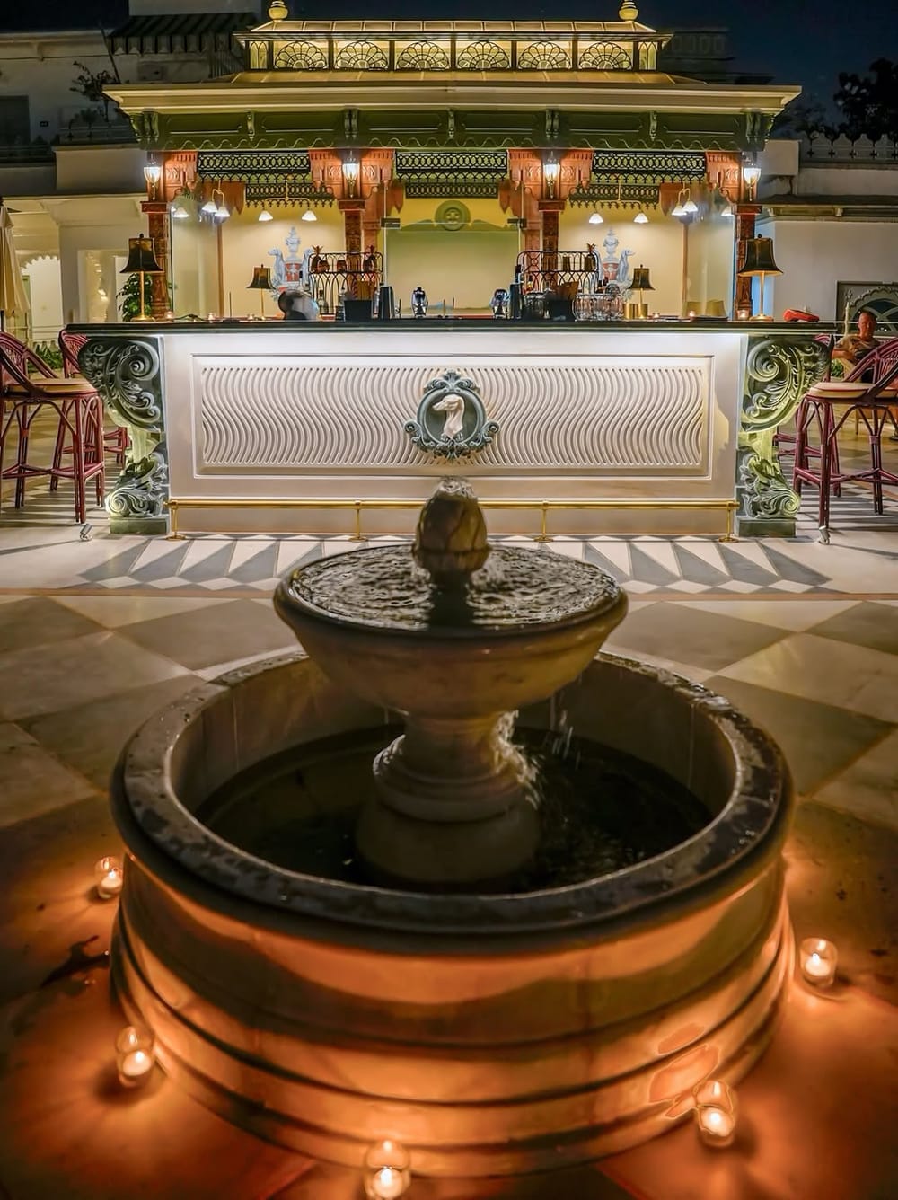 The Ambrai bar at night, a candlelit fountain in front of the carved bar counter