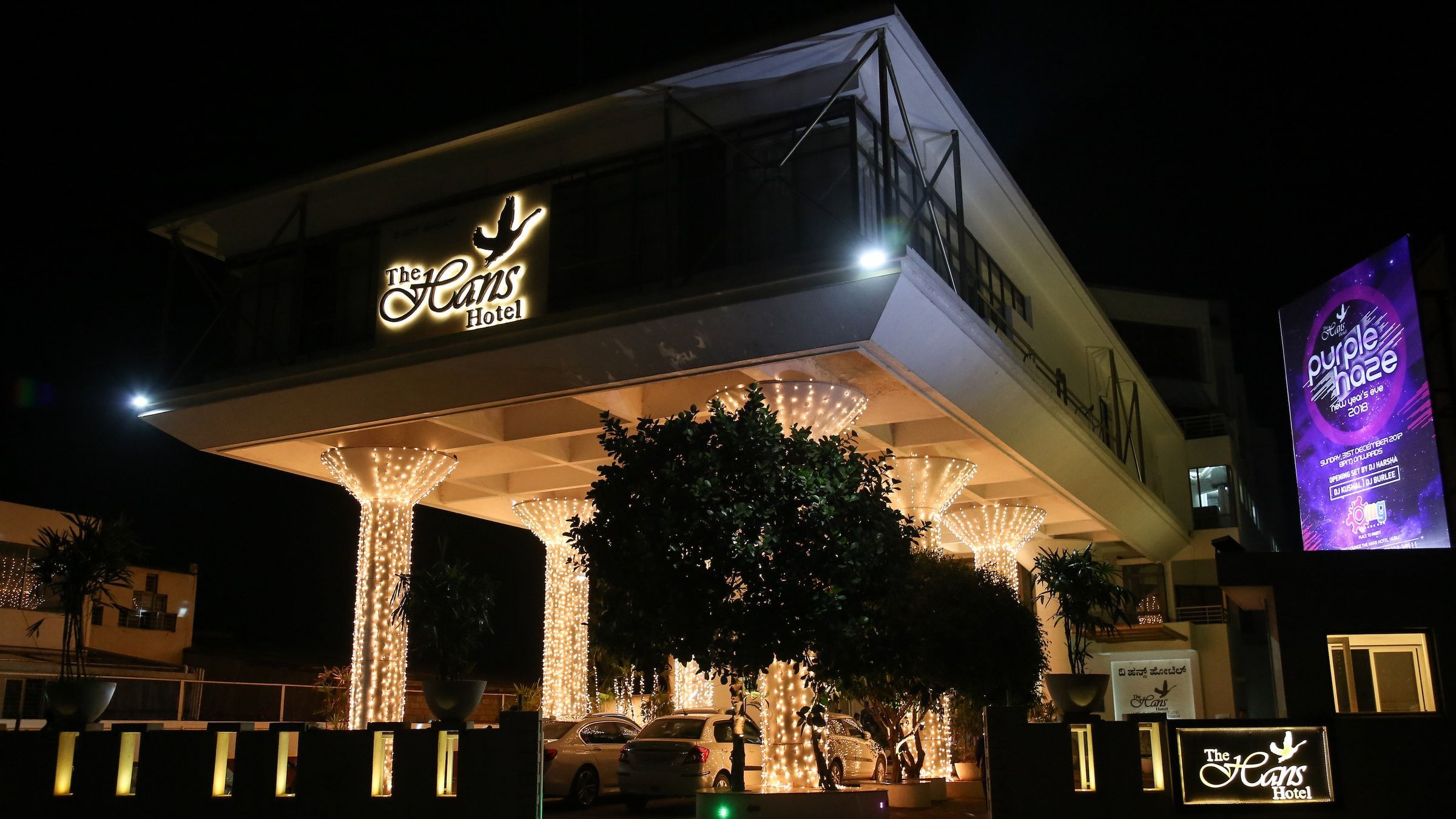 The Hans Hotel porch at night, trees strung with lights beneath the swan emblem