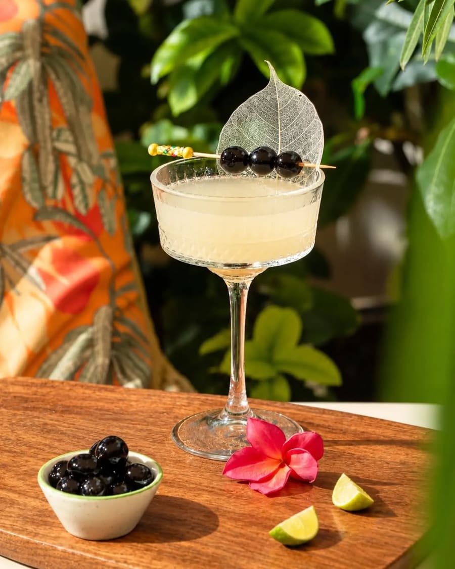 A clear cocktail garnished with a skeleton leaf and cherries