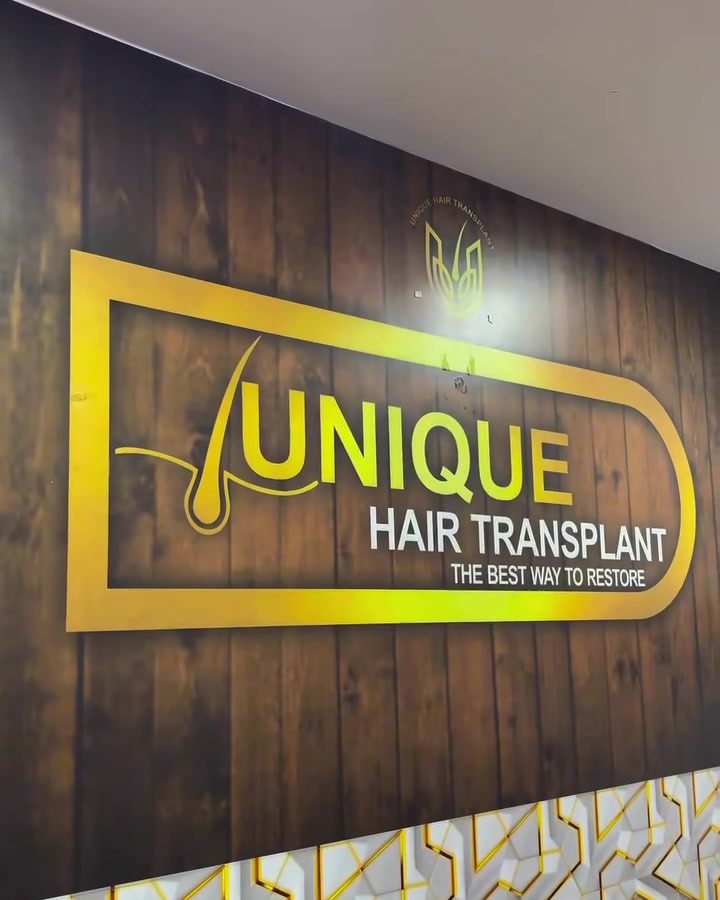 The gold Unique Hair Transplant logo on a wood-panelled wall