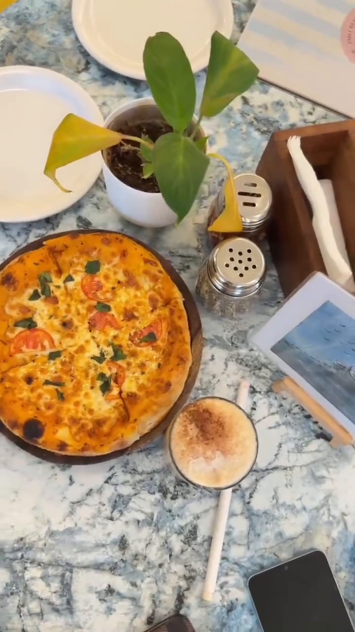 A pizza on a marble table with a cold coffee