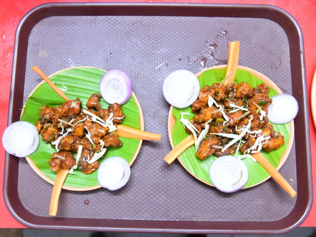 Two plates of fried chicken with onion and lemon on banana-leaf plates