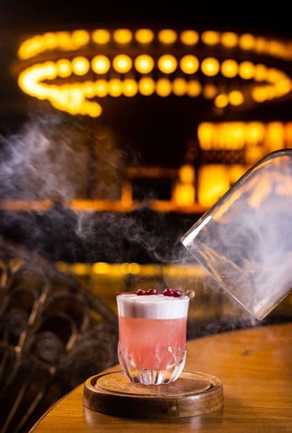 A smoked pink cocktail under a glass cloche