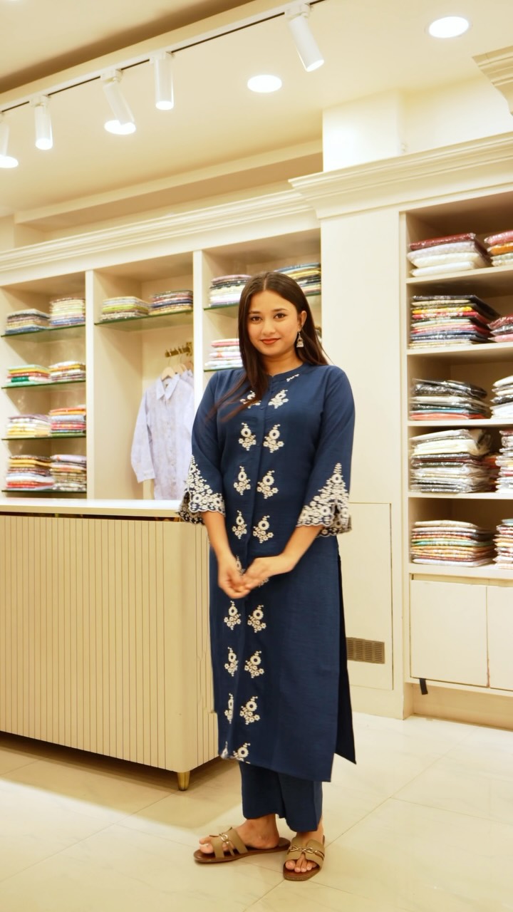 Glass shelves of folded suits behind a model in a navy embroidered kurta