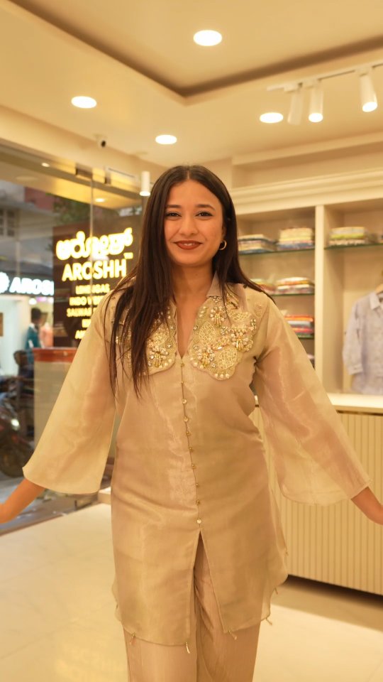 A model in an embellished tissue set beside the glowing Aroshh sign at the boutique entrance