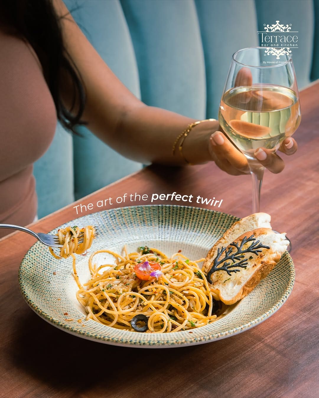 A fork twirling pasta beside a glass of white wine