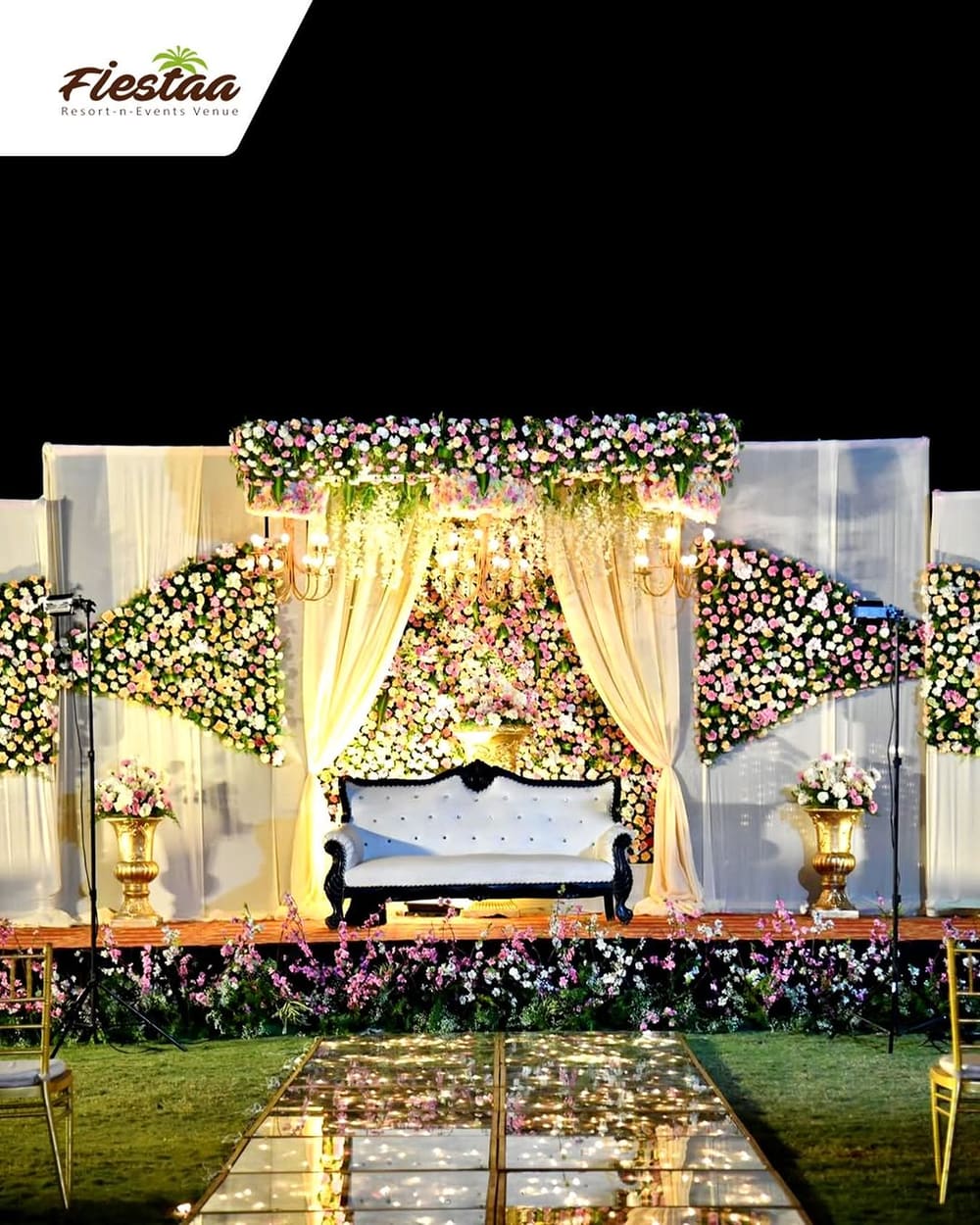 A wedding stage dressed in white florals and chandeliers on the lawn
